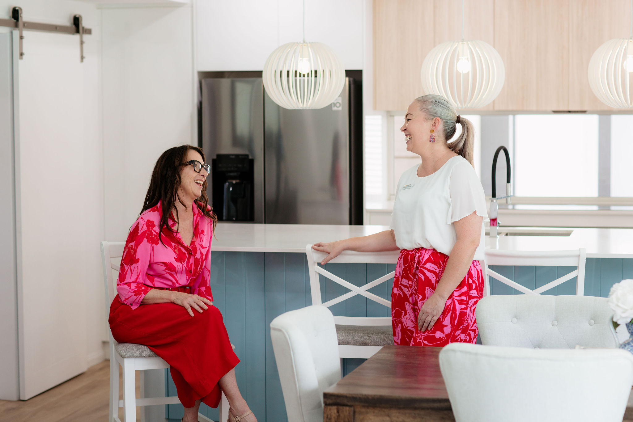 Two Agents in conversation, laughing, in a light coloured kitchen. Agents are dressed professionally. 